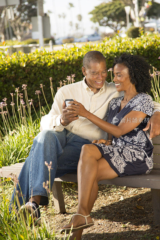 关系:成熟的非洲裔夫妇。公园的长椅上。手机。