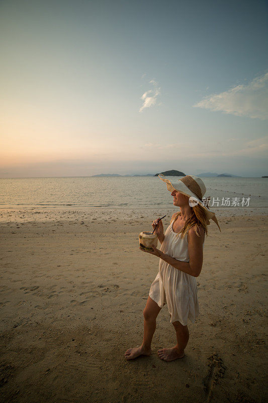 一个手里拿着椰子在海滩上散步的年轻女子