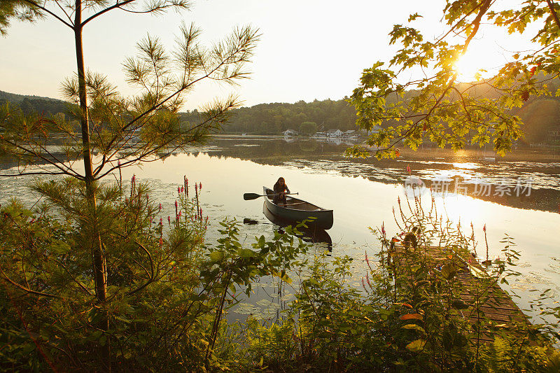日出时小女孩在湖上划着独木舟
