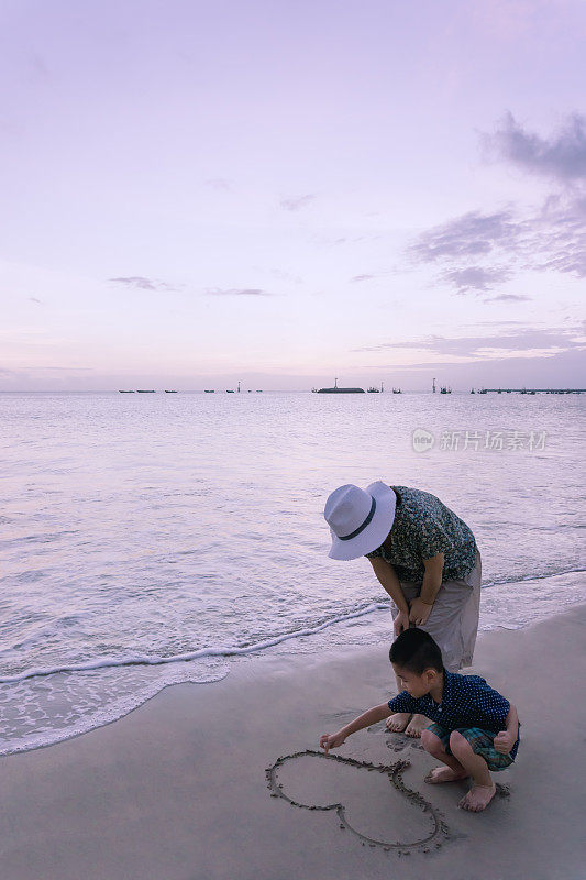 母亲和儿子在海滩上画一颗心