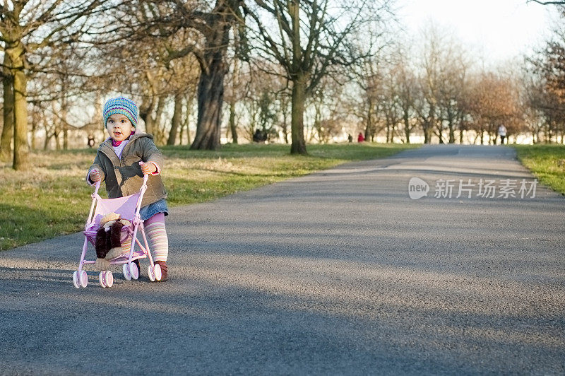孩子在公园里推着玩具婴儿车，水平的