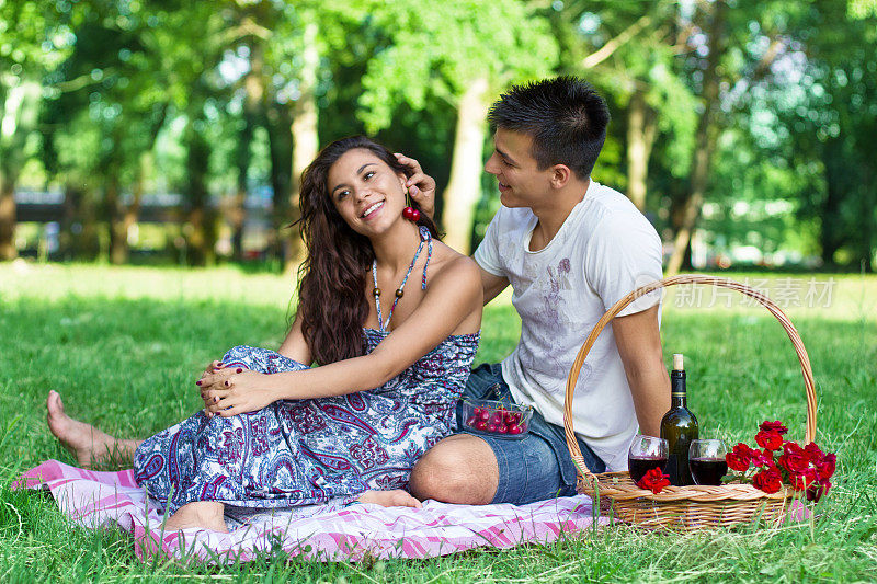 年轻幸福的夫妇在野餐用樱桃模仿耳环