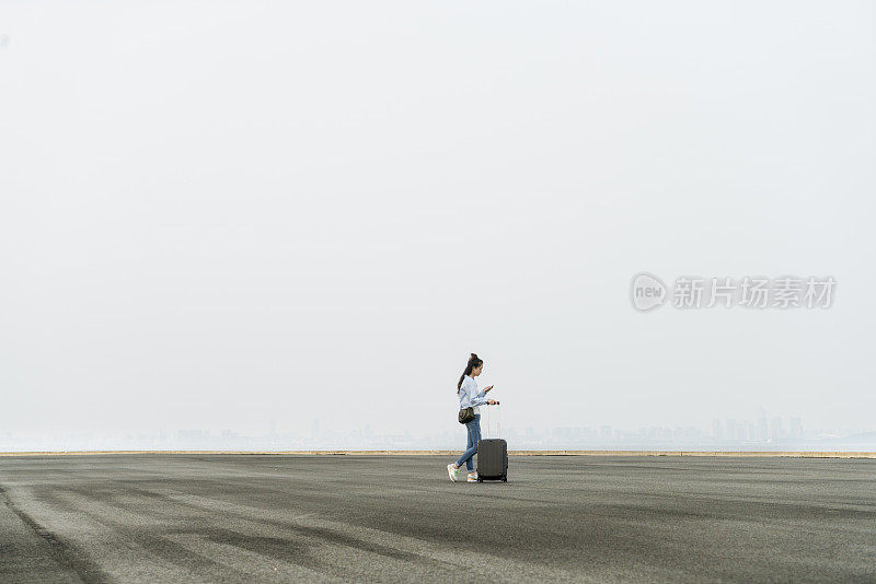 一个年轻女子拖着箱子在天空下走