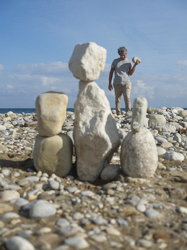 一个艺术家在海滩上布置的石头家庭。艺术家扛着石头建造一个新的人