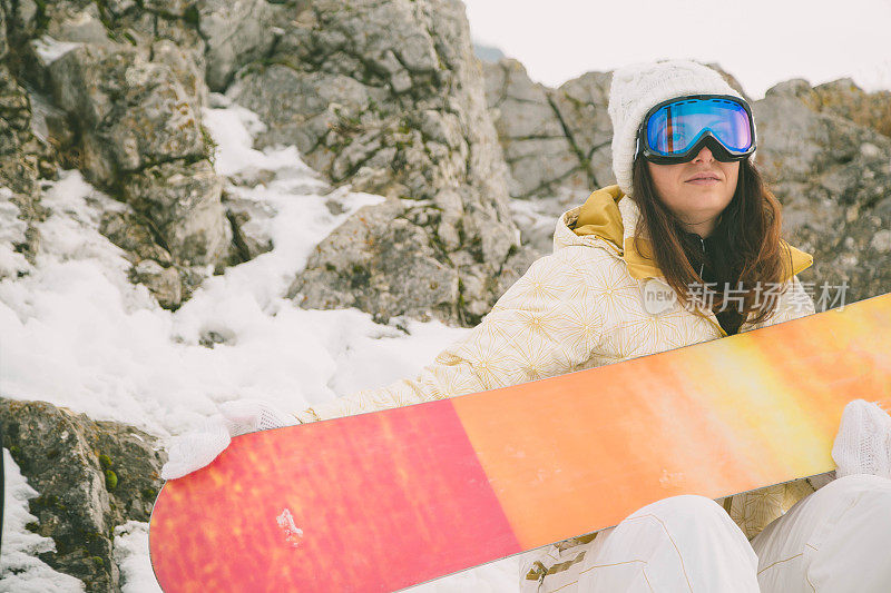 女人拿着滑雪板，背景是高山