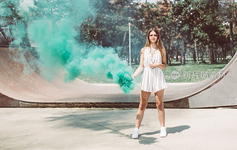 美丽的年轻女孩站在滑板公园和绿色烟雾