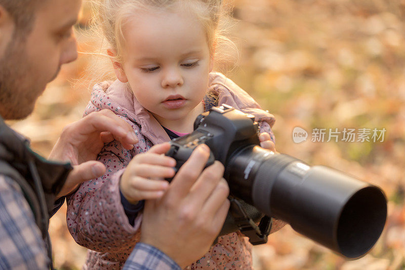 爸爸用专业相机给他可爱的小女儿看照片。