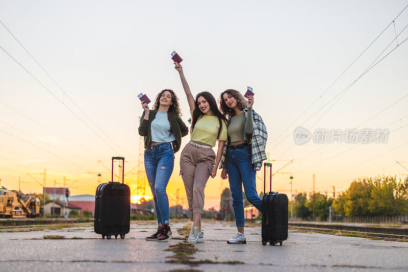 三个快乐的年轻女性朋友在火车站蹦蹦跳跳，因为她们很高兴能够旅行