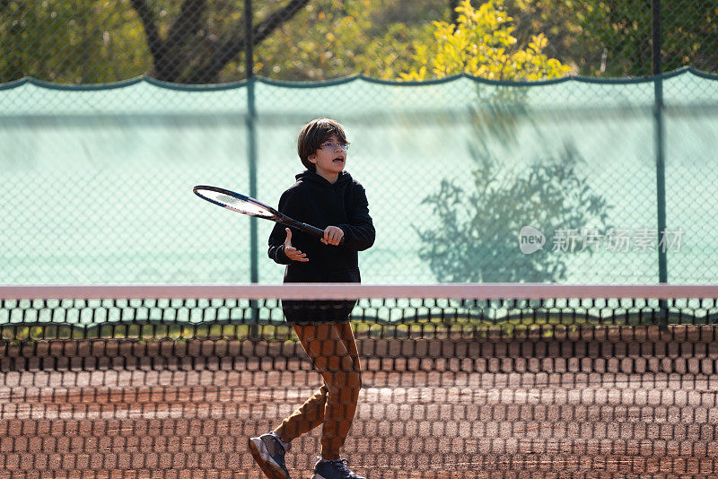 一个男孩正在红土场上打网球。