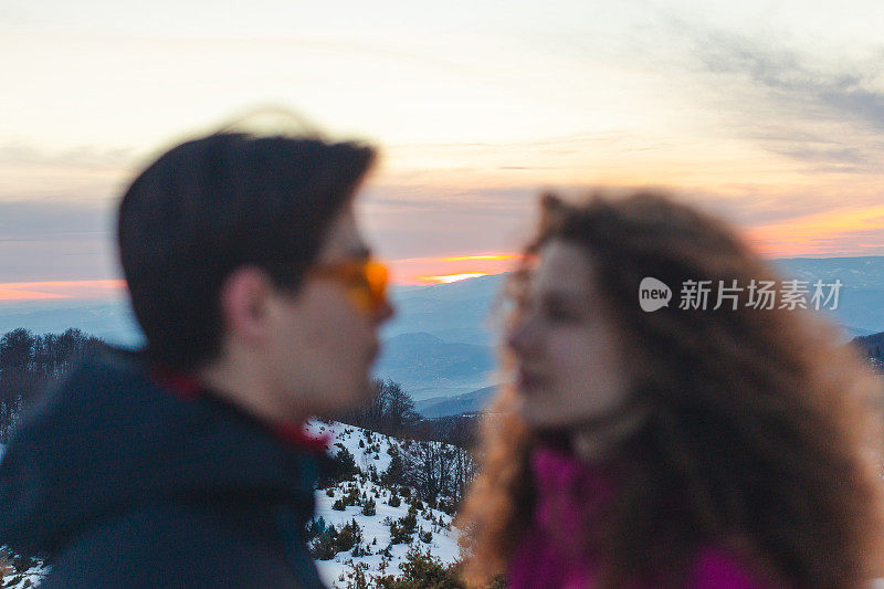 一对美丽的年轻夫妇在雪山的山顶上接吻的特写在他们的滑雪假期