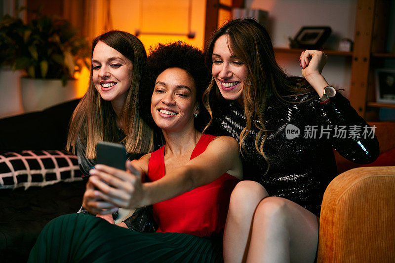 晚上的家庭聚会上，三位多元文化的女性朋友坐在客厅里自拍。