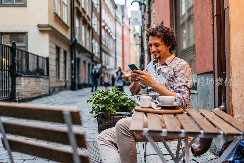 一个年轻人在人行道上喝咖啡和使用手机Café