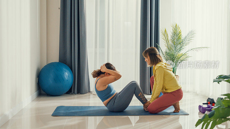 强壮的亚洲运动健身女性在家里客厅的女性私人教练的帮助下工作。