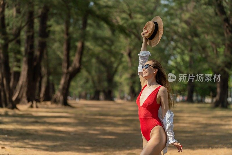 美丽的白人女性性感的女人在红色泳装比基尼寒冷和放松的帽子在她的头上快乐地微笑在森林的海滩