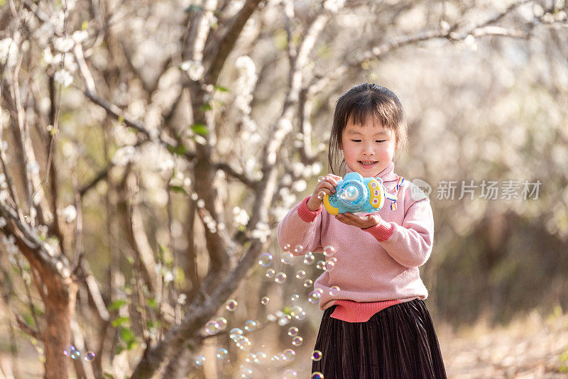 一个小女孩在梅园里玩泡泡机