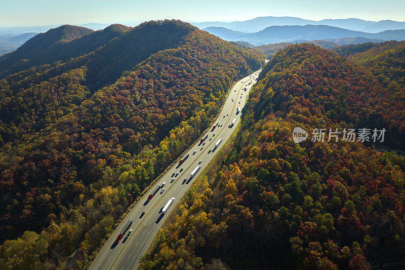 通往北卡罗来纳州阿什维尔的I-40高速公路穿过阿巴拉契亚山口，沿途有黄色的秋天森林和快速行驶的卡车和汽车。高速州际交通的概念