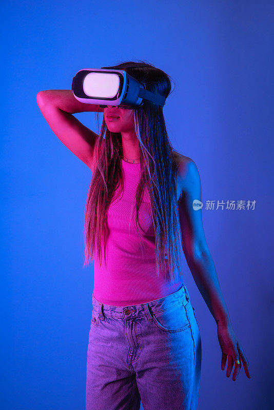戴着现代VR眼镜的女人在工作室里用蓝色和粉红色的霓虹灯探索虚拟现实
