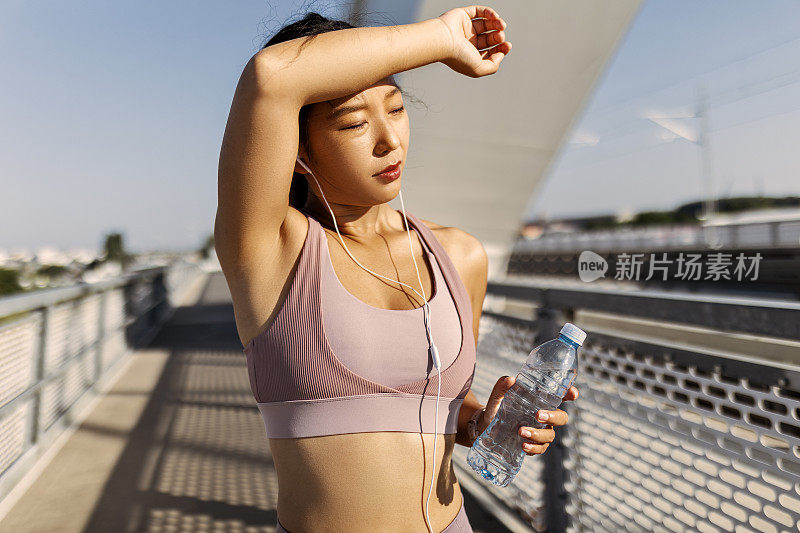 年轻的中国女子在阳光城市桥上锻炼后补充水分