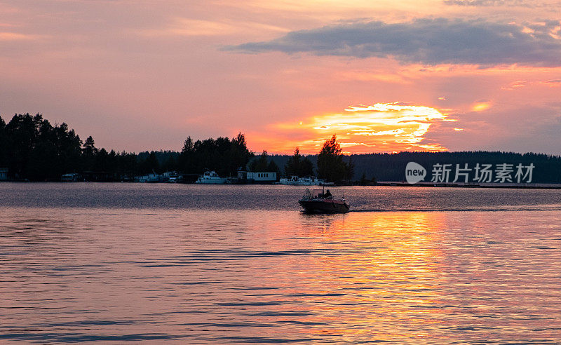 芬兰塞马湖上明亮的夕阳和一艘在夕阳下的机动渔船。夏天的风景