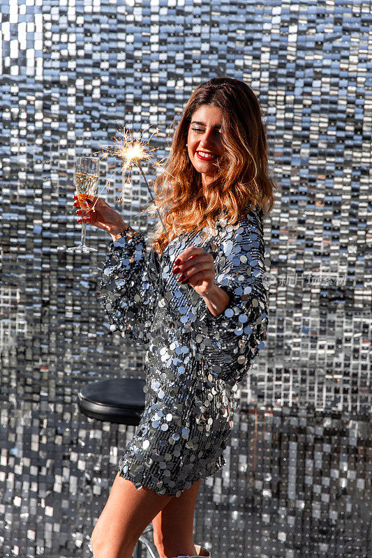 美丽的女人用香槟酒杯和闪闪发光的银白色派对礼服庆祝新年前夜