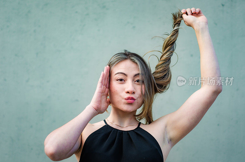 美丽的年轻女子的肖像玩她的头发在灰色背景