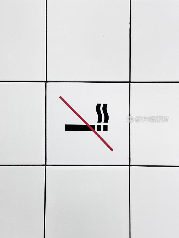 白色禁止吸烟标志标志的特写图像，黑色灌浆的方形系墙，黑色香烟和烟雾标志被红色对角线穿过，重点放在前景上