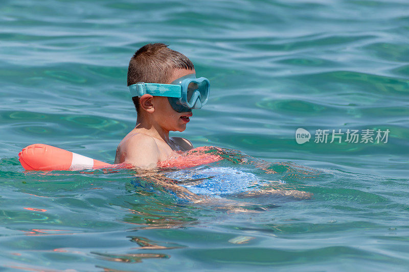 游泳课结束后，戴着泳镜休息的男孩，为了安全，使用漂浮的设备。孩子们在夏季海滩度假时享受水上运动