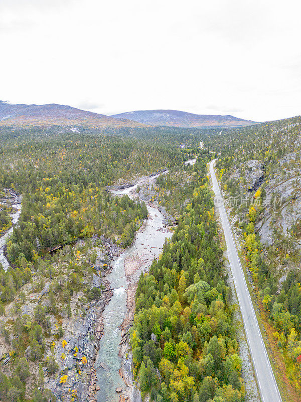 一条宽阔的河流和一条由森林树木和灌木隔开的双车道道路，两边都是岩石