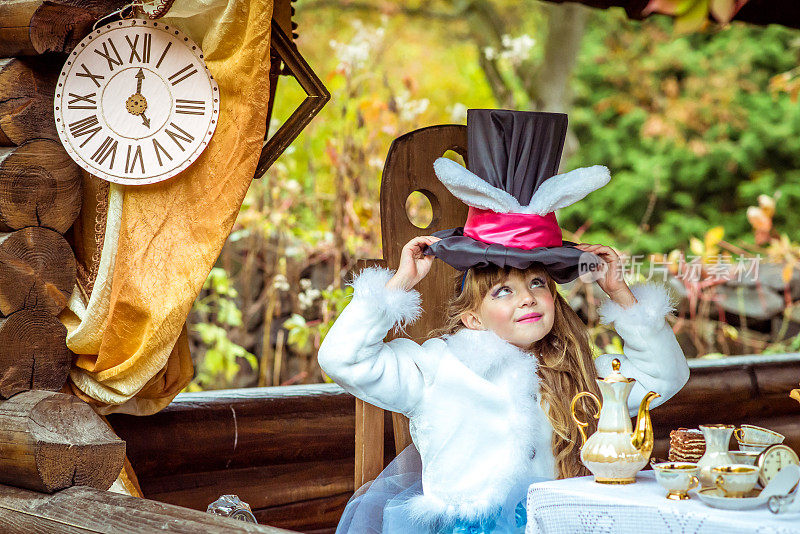 一个漂亮的小女孩拿着一顶长着兔子耳朵的圆柱帽坐在桌子上