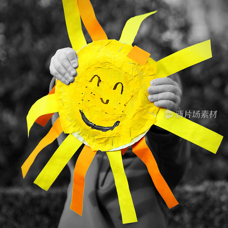 黑白两色的孩子抱着黄色的太阳笑脸