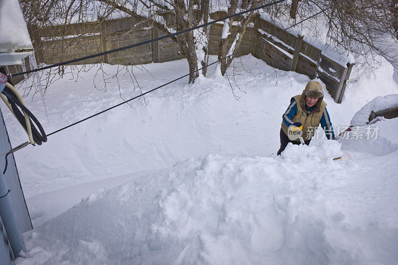 一个成熟的女人从屋顶上铲雪。