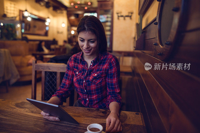 微笑的年轻女子在咖啡厅里使用平板电脑。