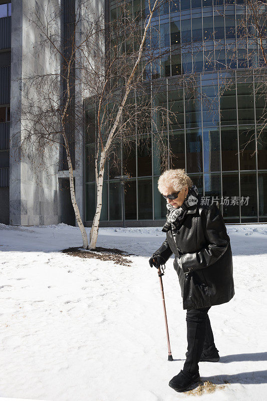 一位老妇人在冬天拄着拐杖走路