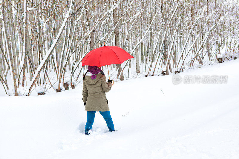 女人撑着红伞走在雪道上