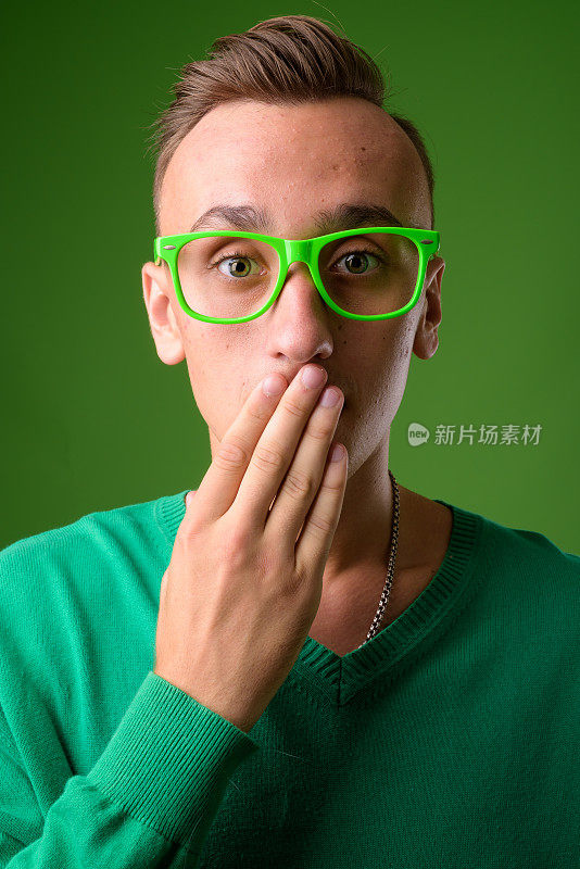 工作室拍摄的年轻英俊的男子穿着绿色毛衣搭配绿色眼镜，以绿色为背景