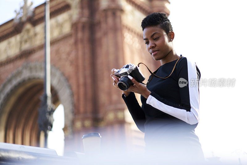 迷人的美国黑人女游客穿着时尚的衣服，用复古相机在城市旅游中拍照，创意的专业女摄影师在阳光明媚的日子里拍摄城市照片