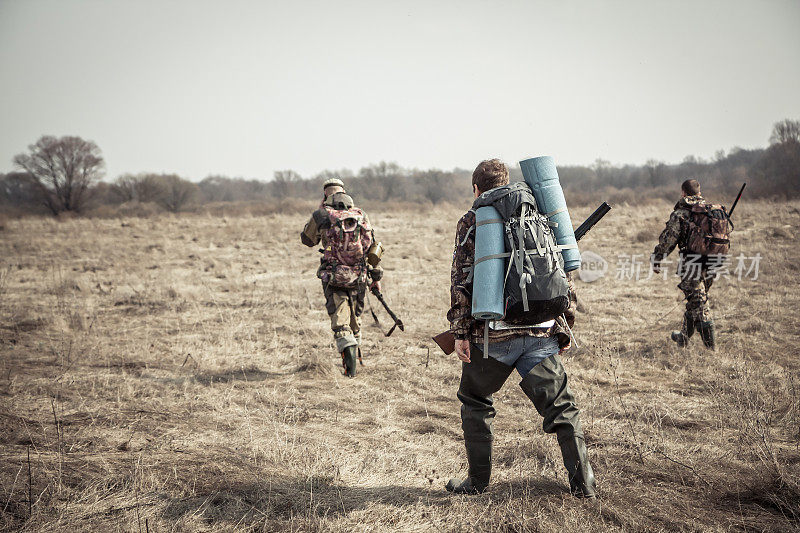 狩猎场景:一群猎人背着背包，背着猎枪，在阴天的狩猎季节穿过乡间田野