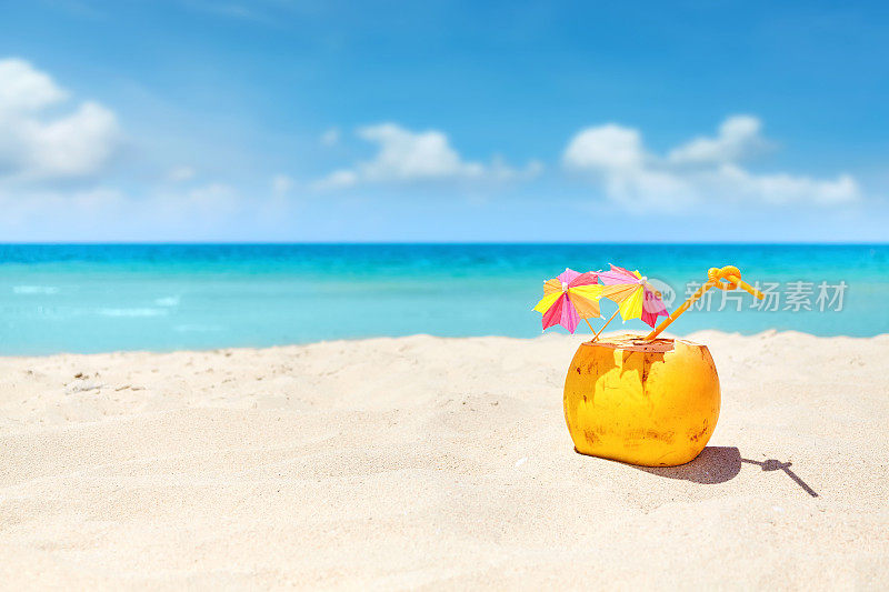 沙滩上的吸管椰子鸡尾酒和五颜六色的雨伞。