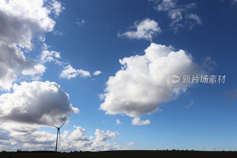 在乡村环境中，蓝天映衬着蓬松的白云，还有风力涡轮机或乡村公路