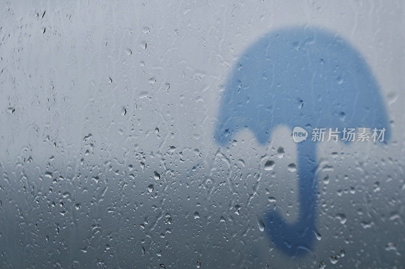 雨伞的剪影在玻璃背景和雨滴。
