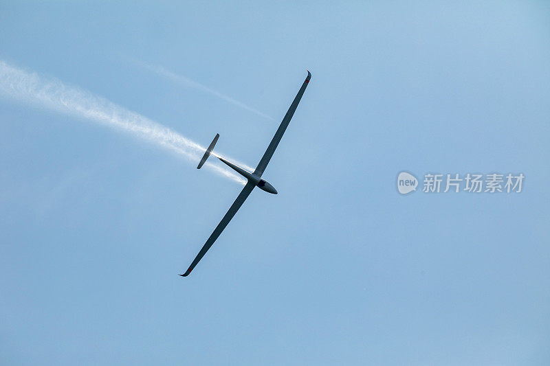 在蓝天上飞行的滑翔机在着陆前喷出水。