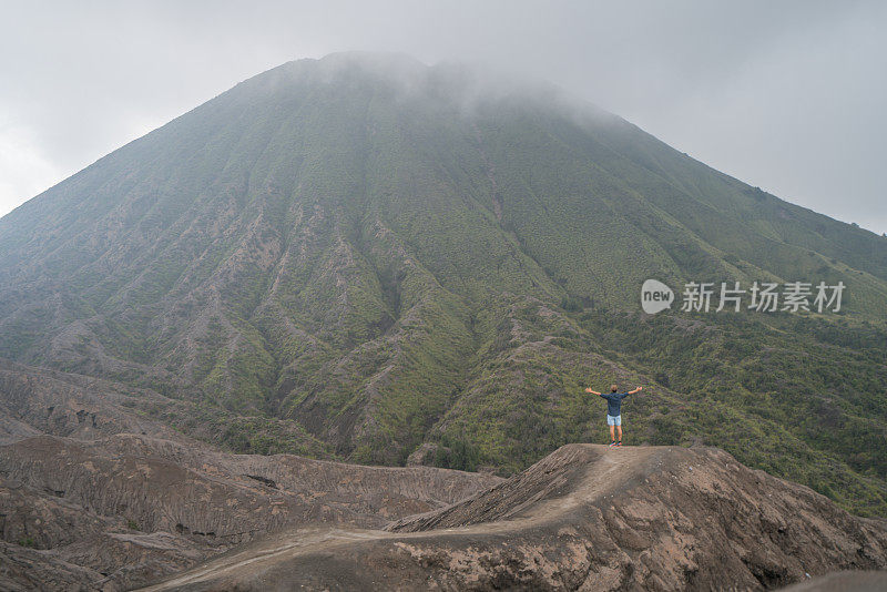 在印度尼西亚，年轻人徒步旅行，手臂伸开站在火山的山顶上，人们旅行的乐趣，冒险的概念，成功和成就