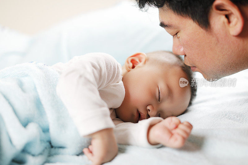 快乐的年轻父亲在熟睡的男婴旁边