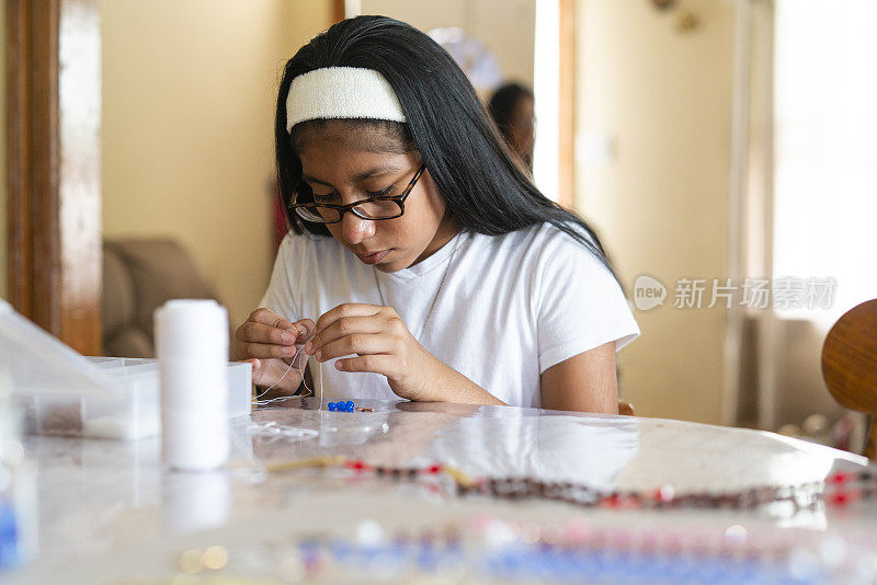 一个严肃的拉丁少女在客厅里做手工，做精美的珠饰