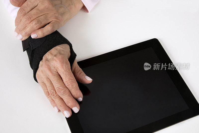 年长妇女爱抚的手与关节炎支架上的电脑平板