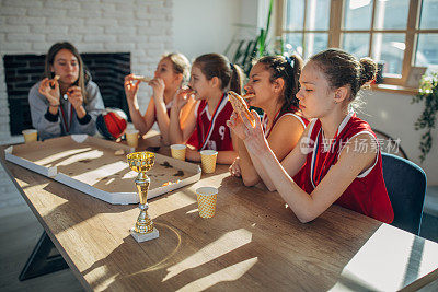 女子篮球运动员在赢得奖杯后和女教练一起吃披萨