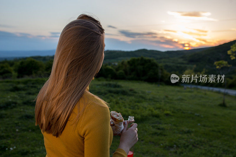 年轻的女性正在吃三明治，享受大自然中的日落