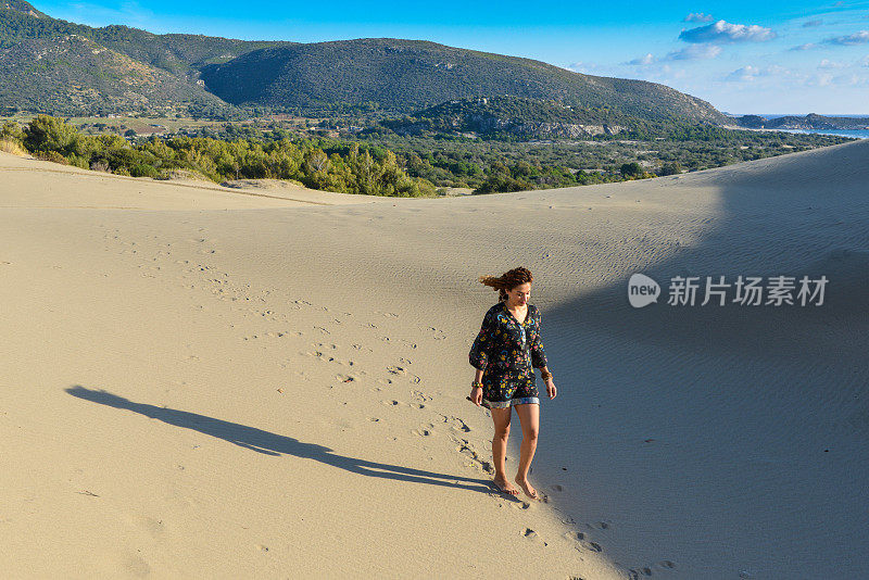 一个年轻漂亮的女人走在沙丘上。