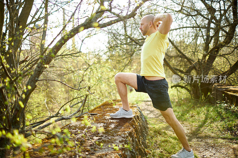 一位中年男子在森林里慢跑，伸伸懒腰，做健身训练