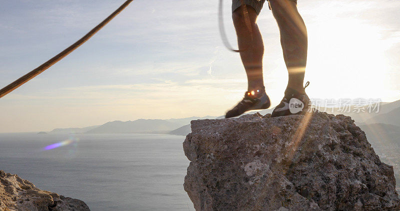日出时攀登者在峰顶的腿的细节